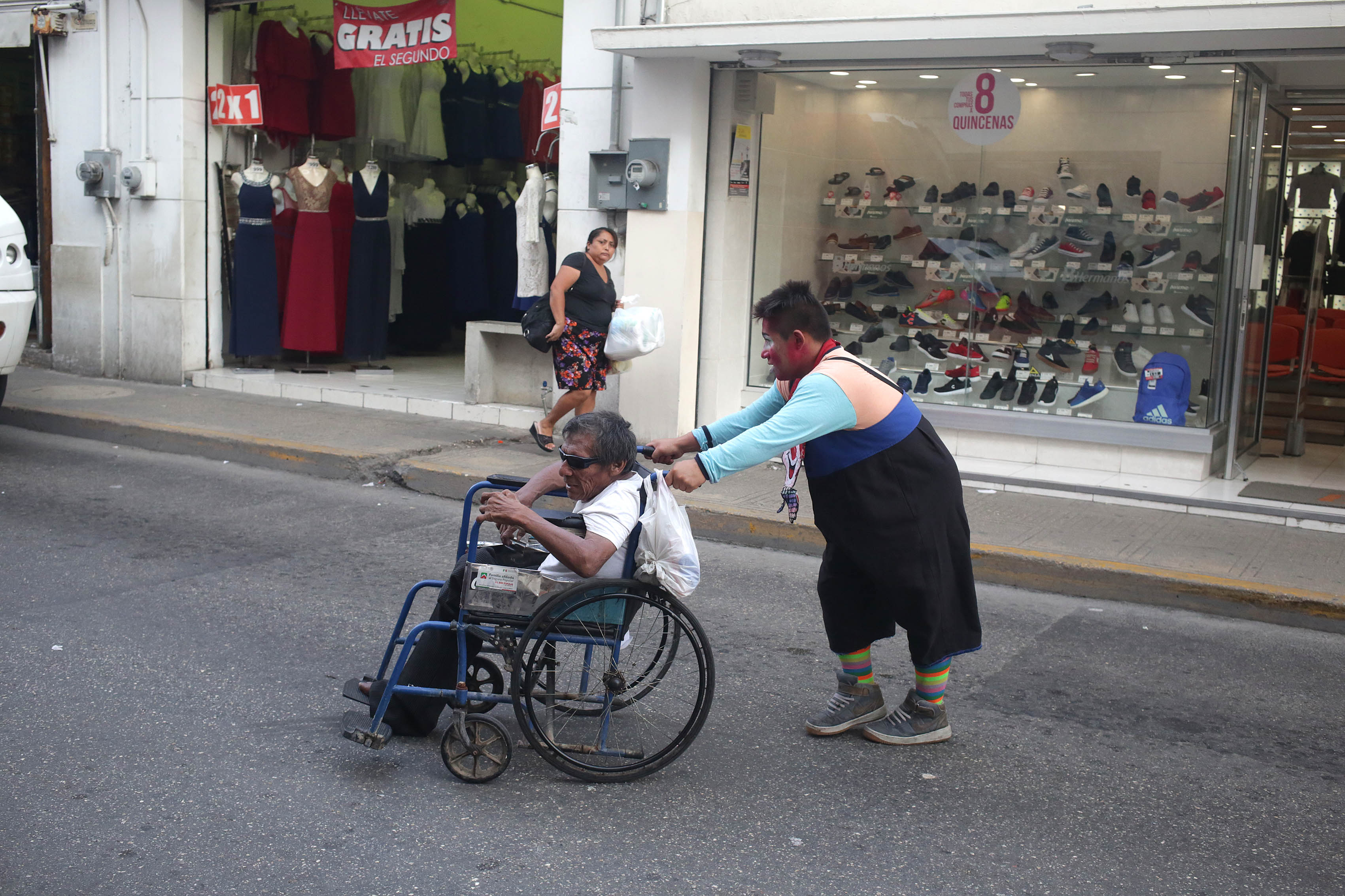 Payaso lleva a hombre en silla de ruedas por calles del centro