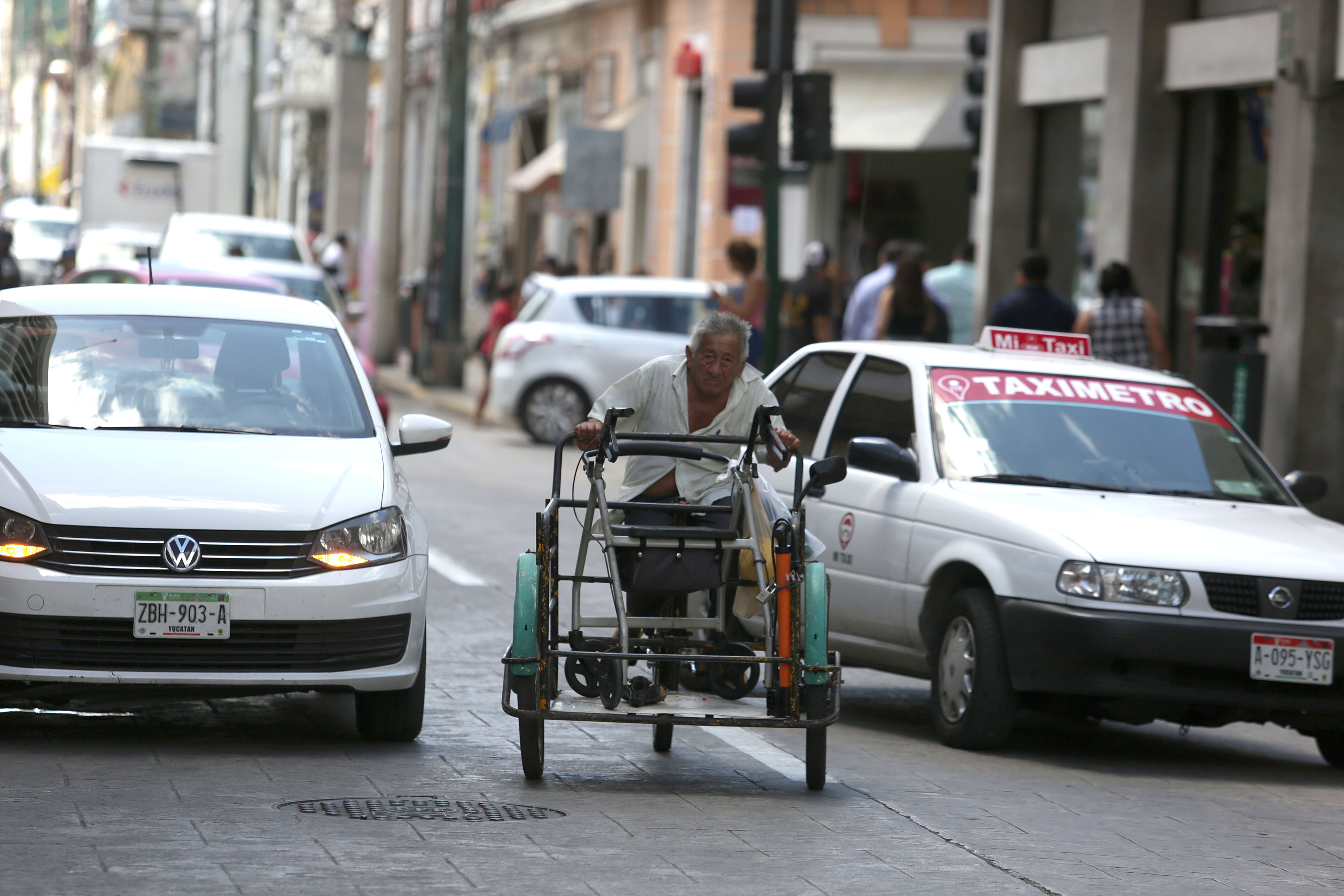 Adulto mayor en triciclo entre dos autos en centro historico