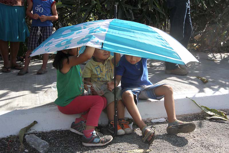 Niños se resguardan del sol debajo de una gran sombrilla